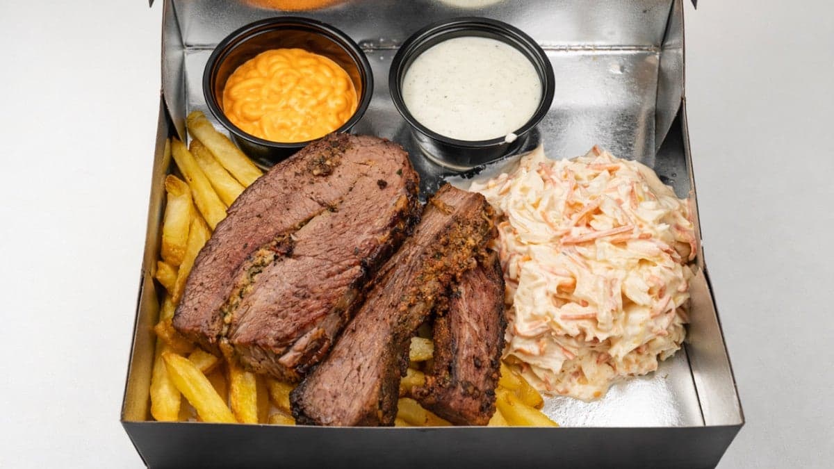 Slow-Smoked Brisket sliced thick in a takeaway box with fries, coleslaw and two house sauces